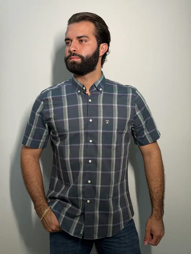 Macro do colarinho button-down de uma camisa xadrez TBull, com as pontas presas por botões em tom osso.