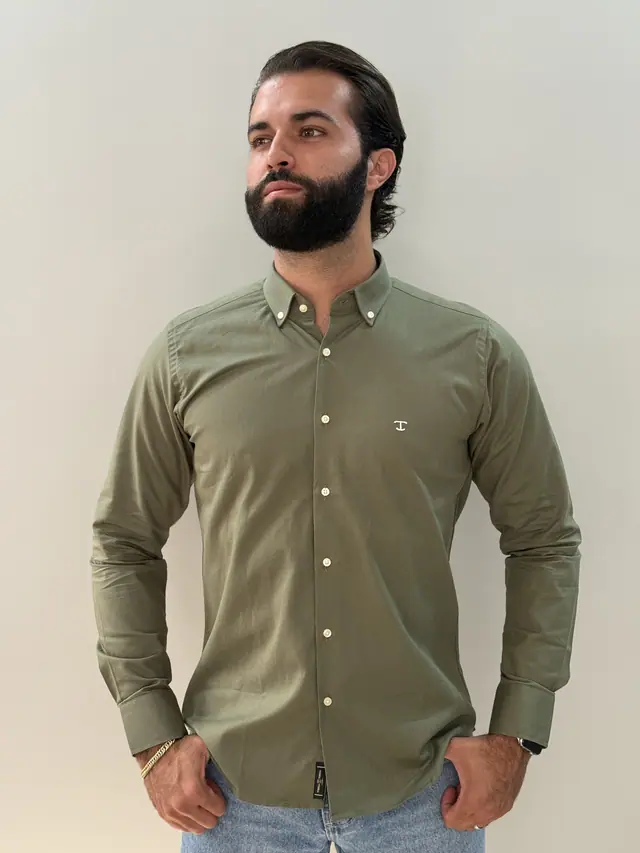 Modelo veste a camisa Militar: verde militar de manga longa, botões em tom osso e monograma no peito.