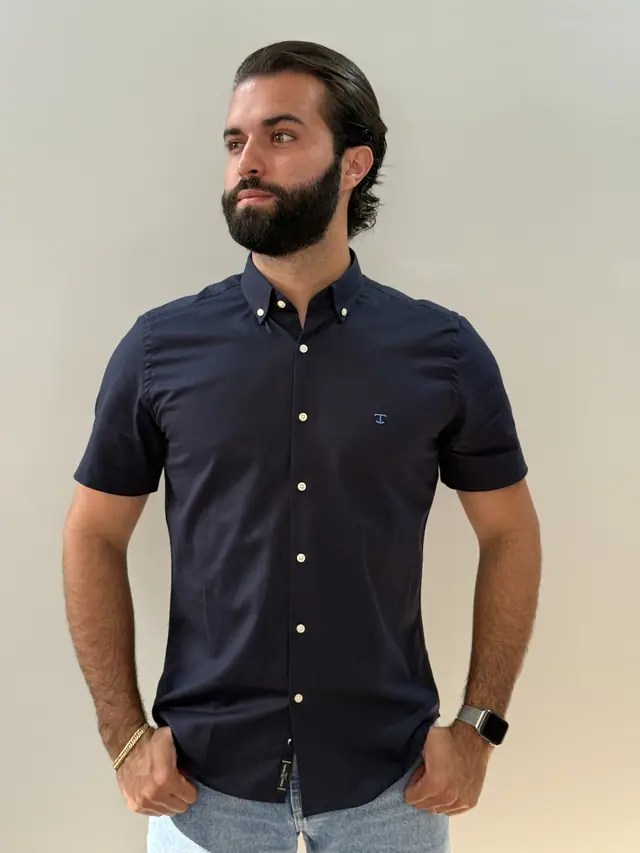 Modelo veste a camisa Marinho OX: oxford azul-marinho de manga curta com botões em tom osso.