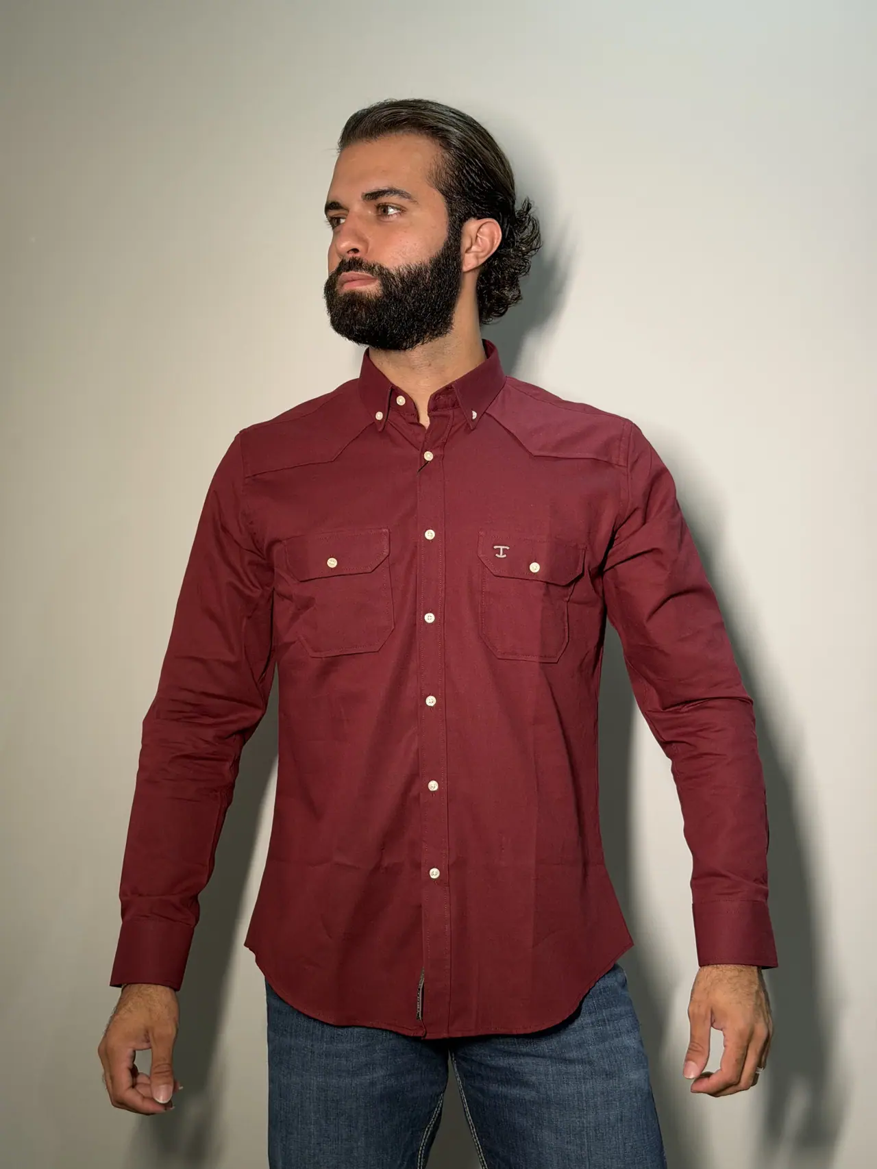 Modelo barbado vestindo a camisa TBull manga longa vinho com bolsos western, canesu, botões em tom osso e monograma T bordado no peito, sobre fundo neutro de estúdio.