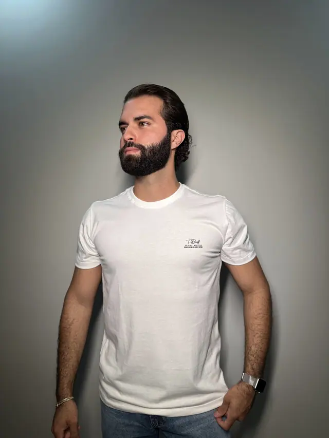 Modelo veste a camiseta Signature: malha off-white de gola careca com a assinatura T·Bull no peito.