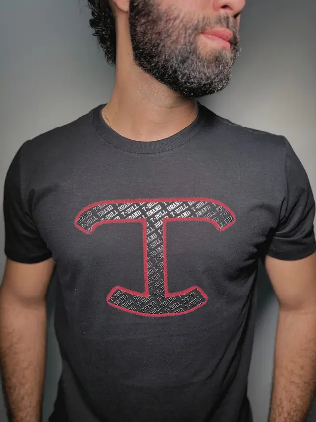 Detalhe do peito da camiseta Rastro: monograma T contornado em vermelho e preenchido por lettering da marca.